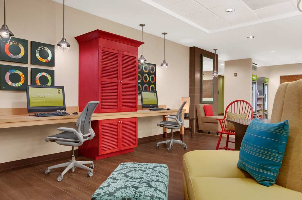 Bright and colorful business center at Home2 Suites in Augusta, Georgia, featuring red cabinetry, modern chairs, and decorative circular wall art. Ideal for guests seeking accommodations near Augusta events.
