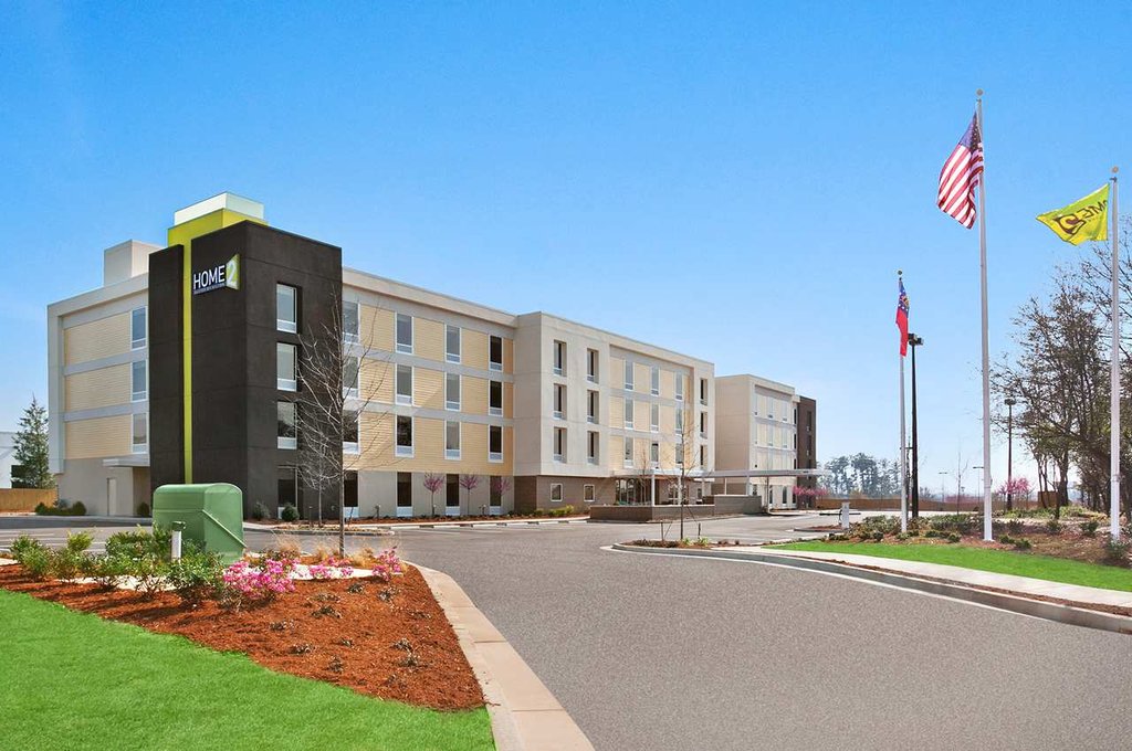 Exterior view of the Hilton Home2 Suites in Augusta, GA, showing a modern hotel building with flags waving and a clear blue sky, located near popular Augusta and Greensboro accommodations.
