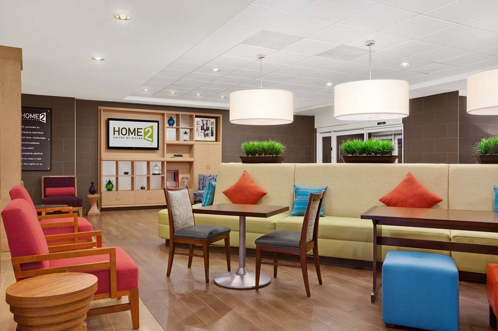 Lobby of Hilton Home2 Suites in Augusta, GA featuring colorful seating areas, large pendant lights, and a visual display with the hotel's branding, ideal for guests visiting the Masters Augusta.