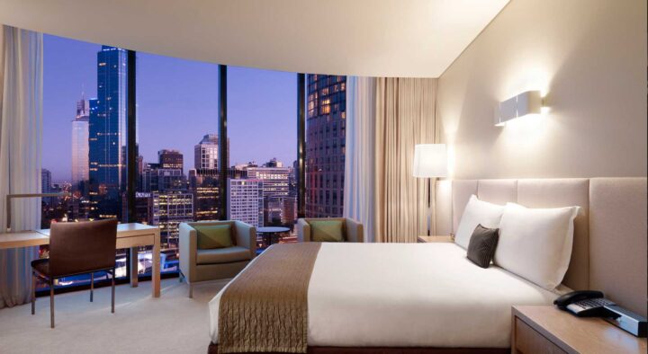 Luxury hotel room with a large bed and panoramic city view through floor-to-ceiling windows, ideal for Australian Open Hotels in Melbourne Park.