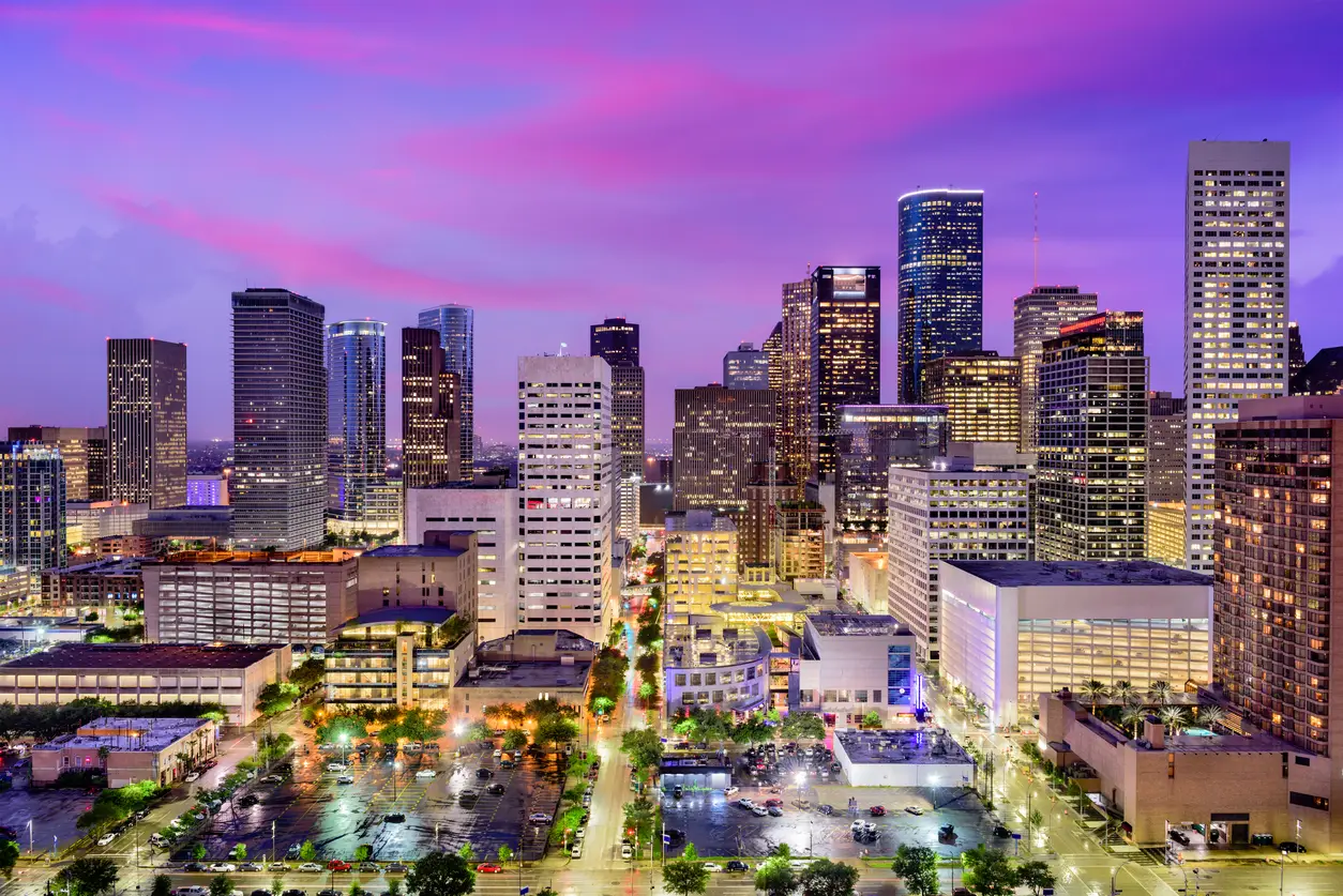 Twilight descends over the vibrant skyline of downtown Houston showcasing lit buildings under a striking pink sky, highlighting its role as a host city for the World Cup.