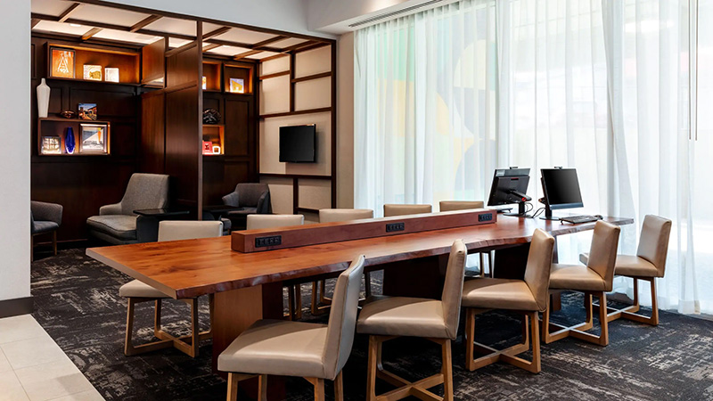Shared computer area at Hyatt Place Atlanta Centennial Park featuring a long table with computers, surrounded by comfortable seating and wooden shelving, ideal for travelers attending World Cup events.