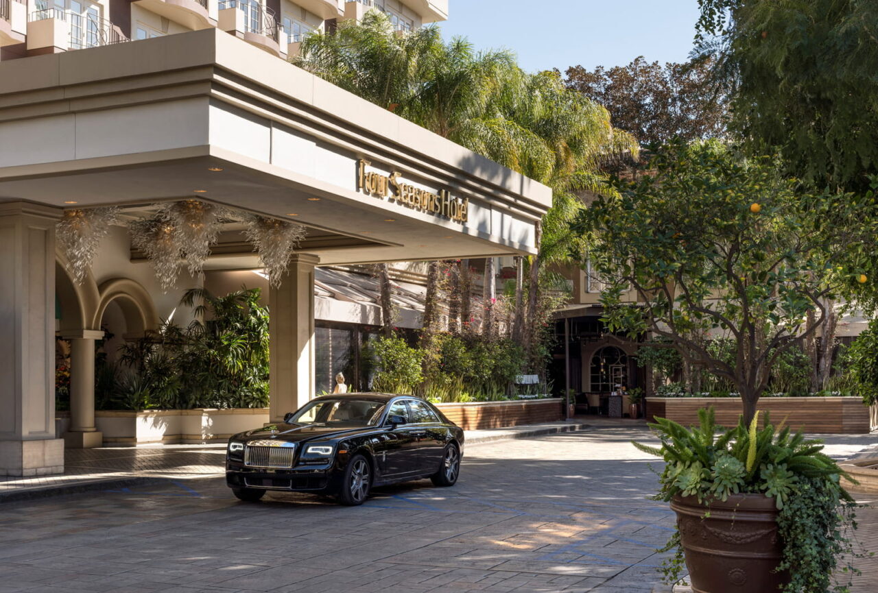 A luxury car parked under the portico of a lush Four Seasons hotel, showcasing an elegant setting for luxury travel and exclusive event hosting.