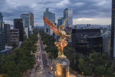 Overlooking Mexico City, the golden Angel of Independence statue stands prominently above a bustling avenue flanked by modern skyscrapers, highlighting the city's status as a host for the World Cup.
