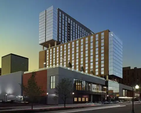 A modern high-rise hotel in Louisville, illuminated at dusk, offering premium Kentucky Derby packages including tickets, travel, and on-site horse farm tours.