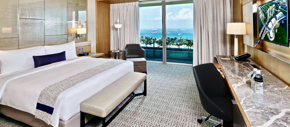 Luxury hotel room in Singapore with a large bed, modern furniture, and a panoramic view of the sea, ideal for visitors attending the Grand Prix.