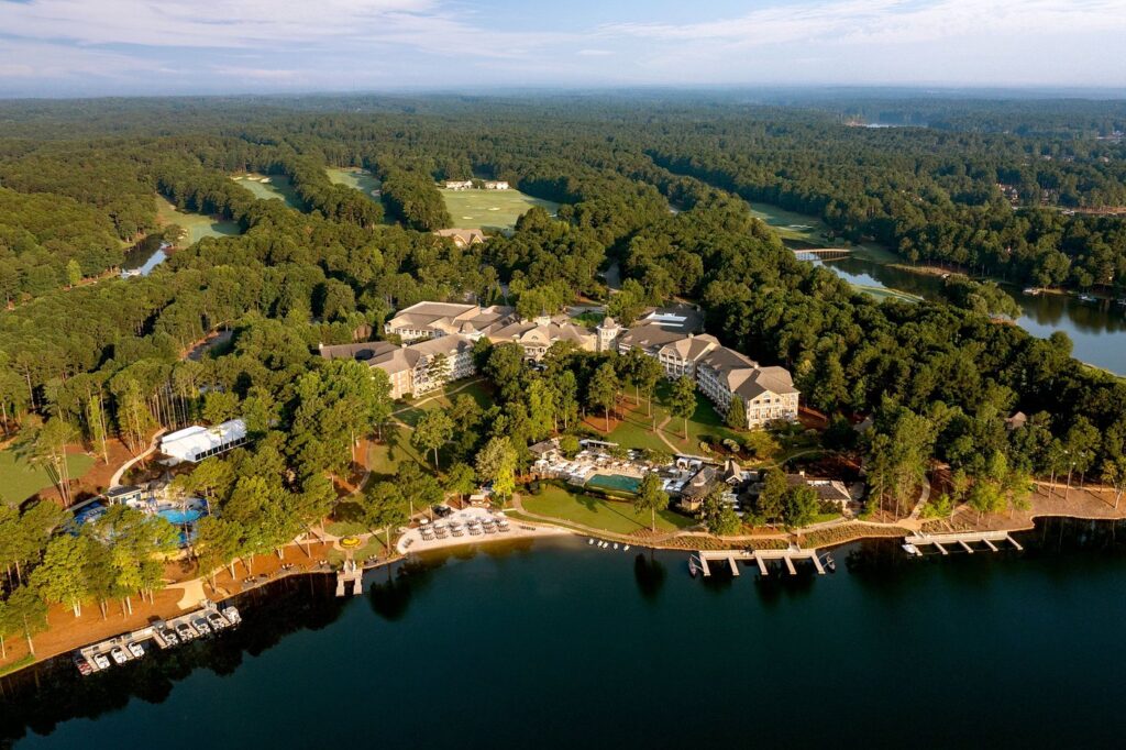 Aerial view of Ritz-Carlton Reynolds at Lake Oconee, showcasing luxurious accommodations and a marina set amidst expansive greens, ideal for Masters Golf Tournament attendees seeking premium hospitality and tours.