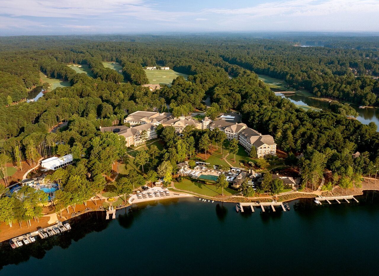 Aerial view of Ritz-Carlton Reynolds at Lake Oconee, showcasing luxurious accommodations and a marina set amidst expansive greens, ideal for Masters Golf Tournament attendees seeking premium hospitality and tours.