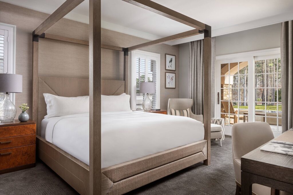 Luxurious bedroom at Ritz-Carlton Reynolds, Lake Oconee, featuring a four-poster bed, elegant furnishings, and natural light from floor-to-ceiling windows, ideal for guests visiting Augusta hotels and accommodations.