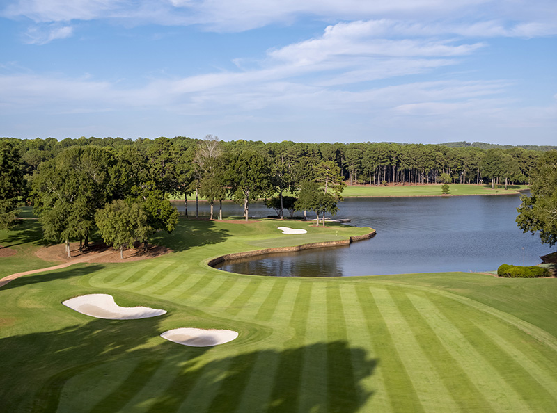 Lush golf course at the Ritz-Carlton Reynolds, Lake Oconee in Greensboro, Georgia, featuring manicured greens, sand bunkers, and a serene lake amidst tall pine trees. Ideal for Augusta Masters accommodations.