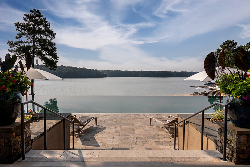 View of Lake Oconee from Ritz-Carlton Reynolds, showing steps leading down to a tranquil lake with umbrellas and lounge chairs, located near Augusta. Ideal for travelers seeking Greensboro and Augusta accommodations.