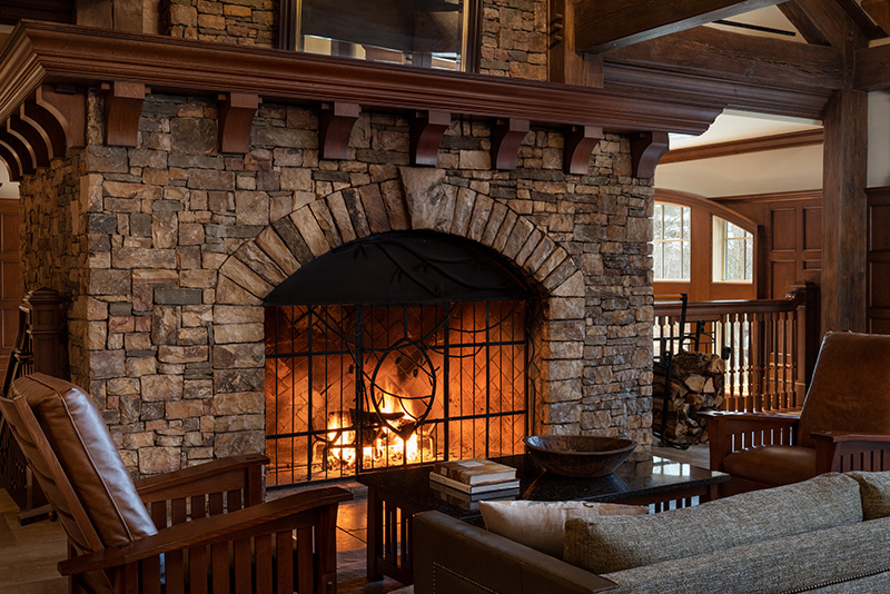 A cozy scene at Ritz-Carlton Reynolds, Lake Oconee featuring a lit fireplace surrounded by stone architecture, wooden furniture, and tasteful rustic decor, ideal for Augusta Hotels near Greensboro.