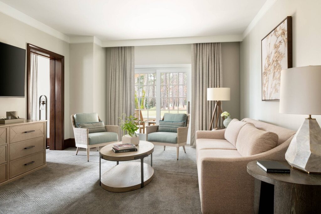 Elegant suite living room at The Ritz-Carlton Reynolds, Lake Oconee, featuring a plush sofa, two armchairs, and a view of greenery outside, ideal for visitors seeking Augusta hotel accommodations.