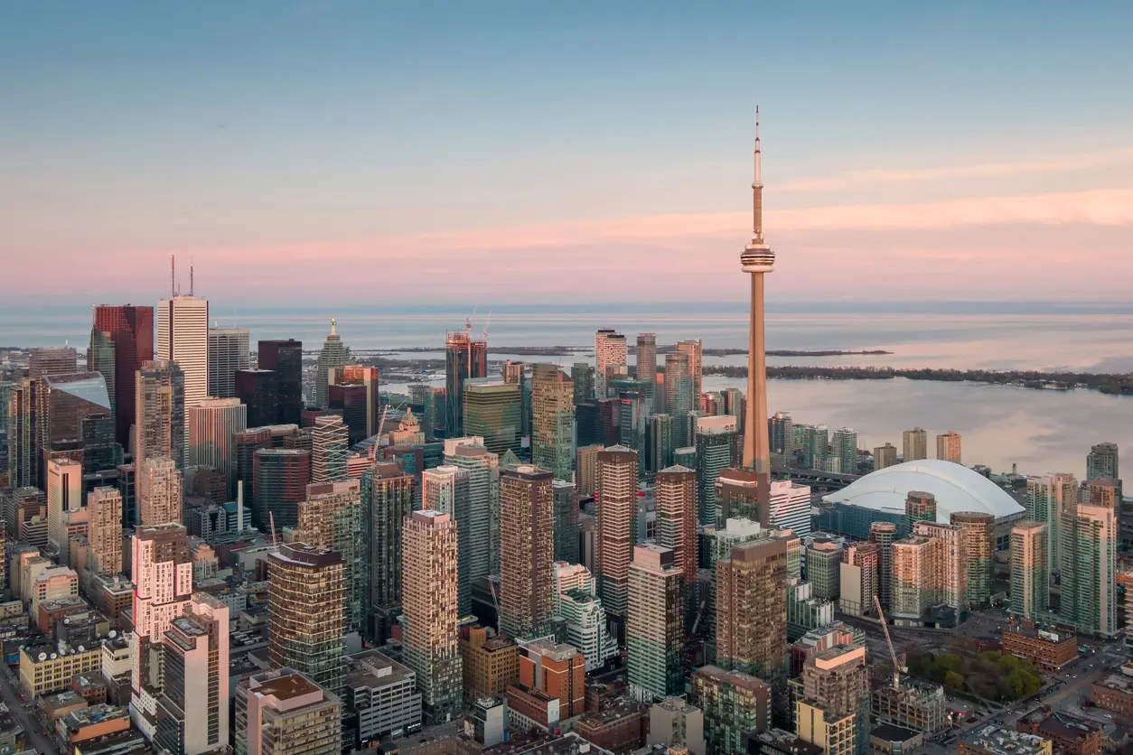 Aerial view of downtown Toronto featuring the iconic CN Tower amid a dense skyline of high-rise buildings, with Lake Ontario in the background.