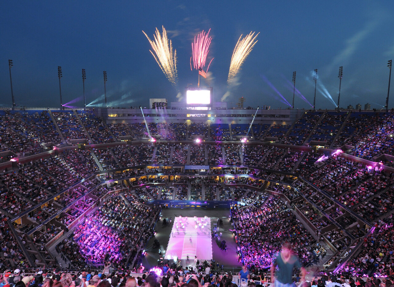 Fireworks light up the night sky above a packed stadium during the opening ceremony of a US Open Tennis event, showcasing the custom US Open Tennis Packages available.