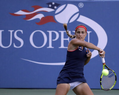 Female tennis player in action at the US Open, hitting a forehand against a backdrop featuring the event's logo, highlighting the intensity of custom US Open Tennis Packages.