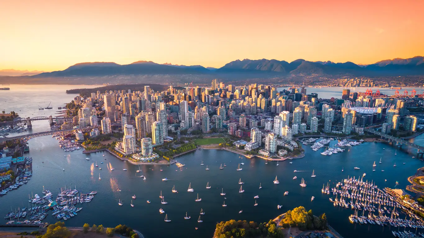 Sunset view over Vancouver showing dense high-rises and the BC Place Stadium, a venue for the World Cup, nestled between the ocean and mountains.
