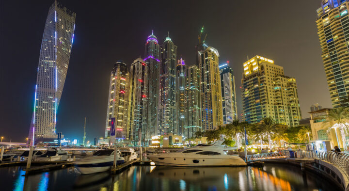 Night view of illuminated skyscrapers in Abu Dhabi near marina filled with yachts, promoting the Abu Dhabi Grand Prix and connecting the experience of road trips and discovery.