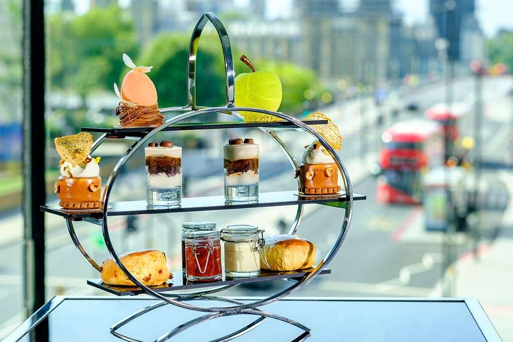 Elegant afternoon tea setup featuring various desserts on a tiered stand with a backdrop of London streets, ideal for luxury accommodations near the Wimbledon Championships.