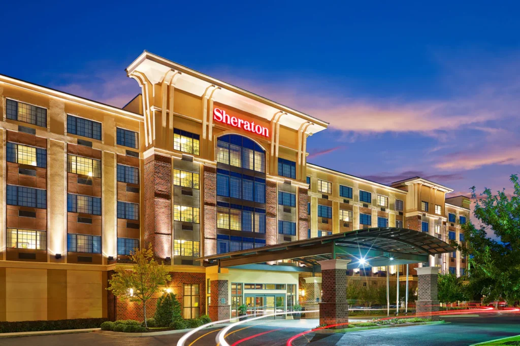Twilight view of Sheraton Augusta Hotel, featuring illuminated signage and a vibrant sky, ideal for guests attending Masters in Augusta, GA.