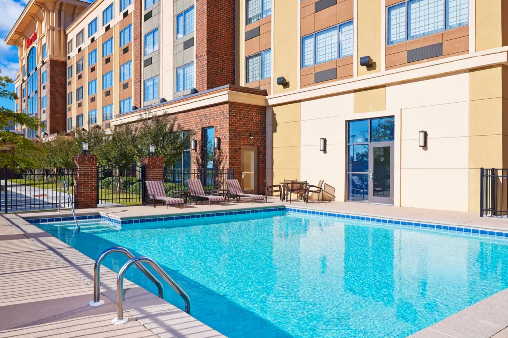 Outdoor swimming pool at a hotel in Augusta, Georgia, showing deck chairs and a multi-story building in the background, ideal for Masters accommodations in Augusta.
