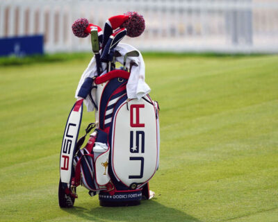Golf bag with 'USA' branding and golf clubs on a green course, signifying the Ryder Cup in Long Island, New York, part of a luxury travel package.