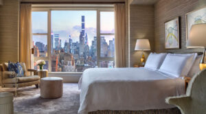 A luxurious hotel room with a large bed, elegant furniture, and an expansive view of the New York City skyline from the window, ideal for World Cup accommodations.
