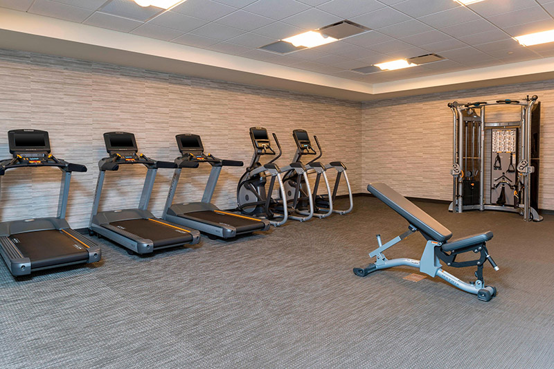 Well-equipped gym at the Courtyard by Marriott Louisville Downtown, featuring treadmills, elliptical machines, a weight training station, and a bench, ideal for visitors attending the Kentucky Derby.