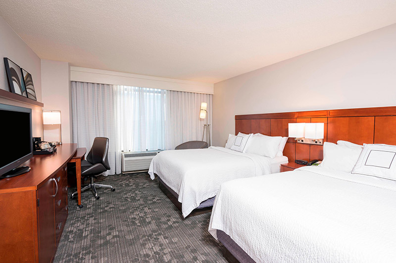 Interior of a well-appointed hotel room at the Courtyard by Marriott Louisville Downtown, featuring two queen beds, a work desk, and a large window; perfect for visitors attending the Kentucky Derby.