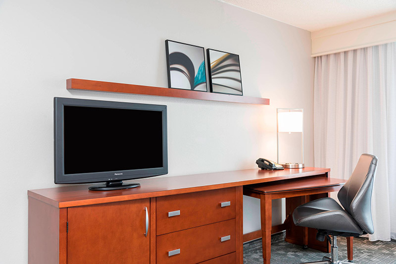 Interior of a modern hotel room featuring a desk, leather chair, flat-screen TV, and art pieces, located at Courtyard by Marriott Louisville Downtown, convenient for Kentucky Derby visitors.