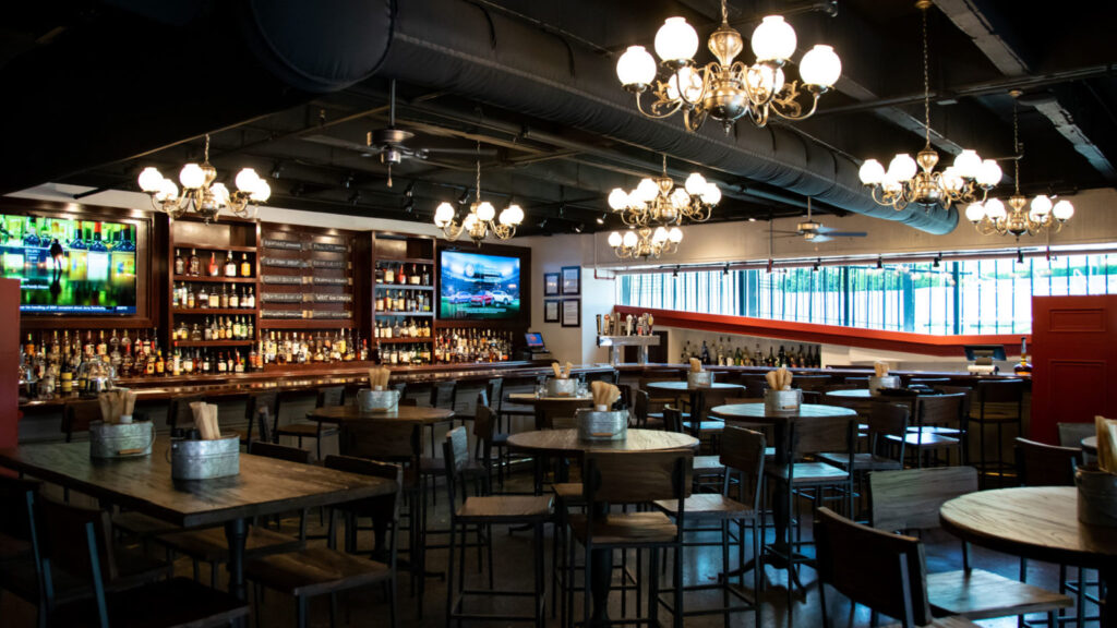 Well-lit bar with multiple wooden tables and a large liquor display, showcasing a luxurious yet cozy ambience, ideal for visitors looking for luxury hotels near Churchill Downs.