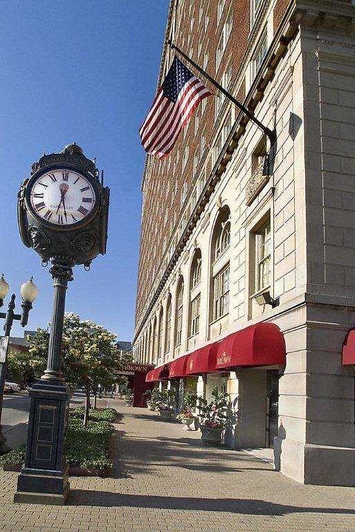 Street view of The Brown Hotel in Louisville, Kentucky, featuring a prominent street clock, an American flag, and red awnings, ideal for visitors to the Kentucky Derby near Churchill Downs.