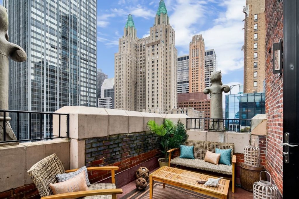 Cozy rooftop patio setup with wicker furniture and cushions overlooking towering skyscrapers in New York, near the Lexington Hotel, ideal for visitors of the US Open Tennis.