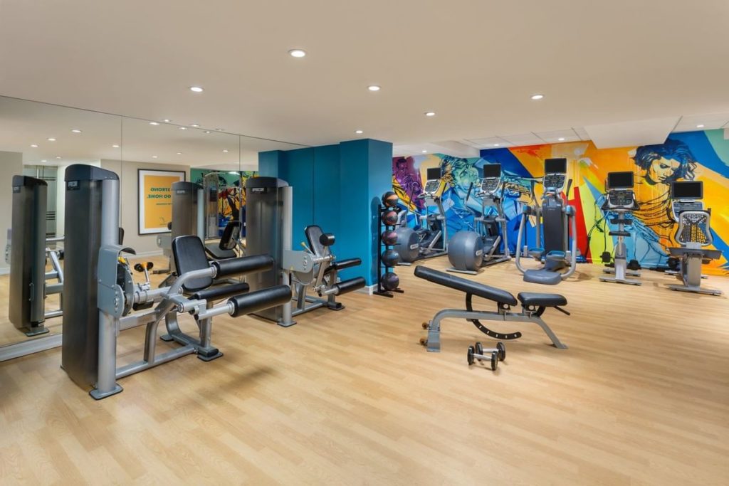 A modern gym equipped with various exercise machines and vibrant, colorful wall art, located at The Lexington Hotel, Autograph Collection in New York. Ideal for guests visiting the US Open Tennis.