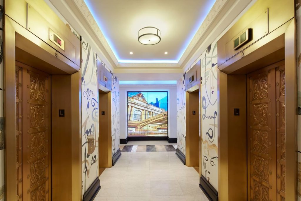 Elevator lobby in the Lexington Hotel, Autograph Collection, featuring ornately decorated doors and a vibrant, illuminated display at the end of the hallway, ideal for guests visiting New York for the US Open Tennis.