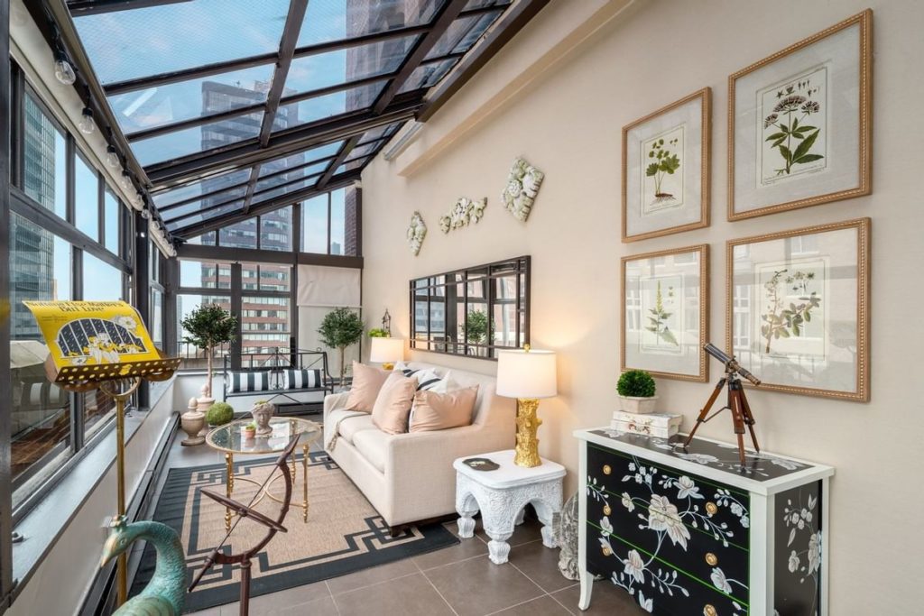 A luxurious sunroom features a comfortable seating area, glass ceiling, botanical artwork, and urban views, likely in a hotel near the US Open Tennis event in New York.
