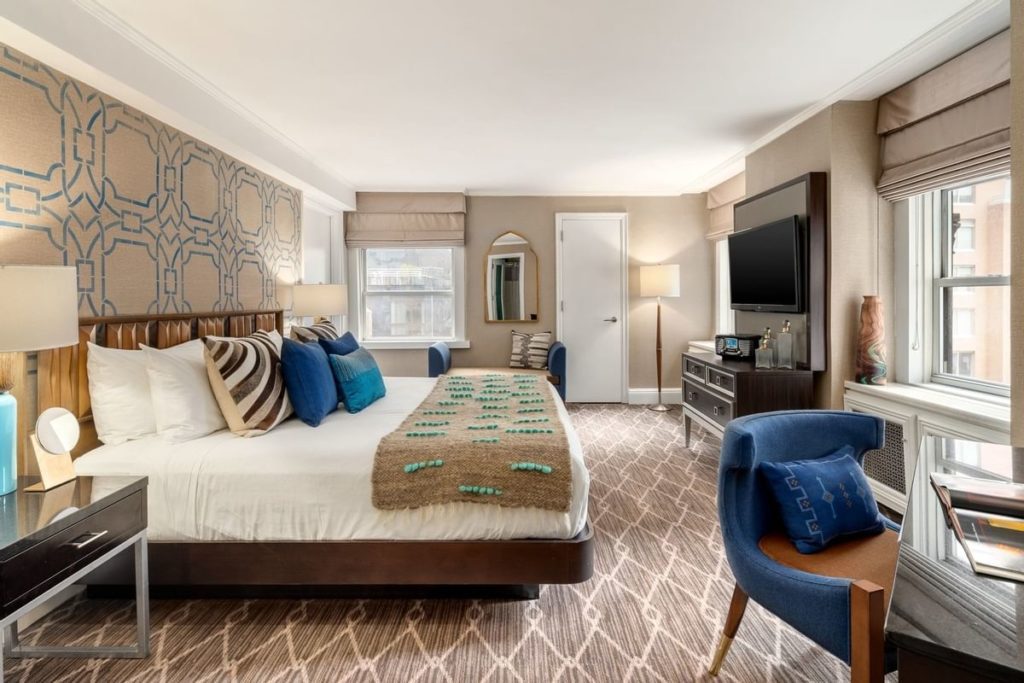 Bright and stylish hotel room at The Lexington Hotel, Autograph Collection in New York, featuring a king-sized bed, decorative accent wall, and modern furnishings, ideal for US Open Tennis visitors.