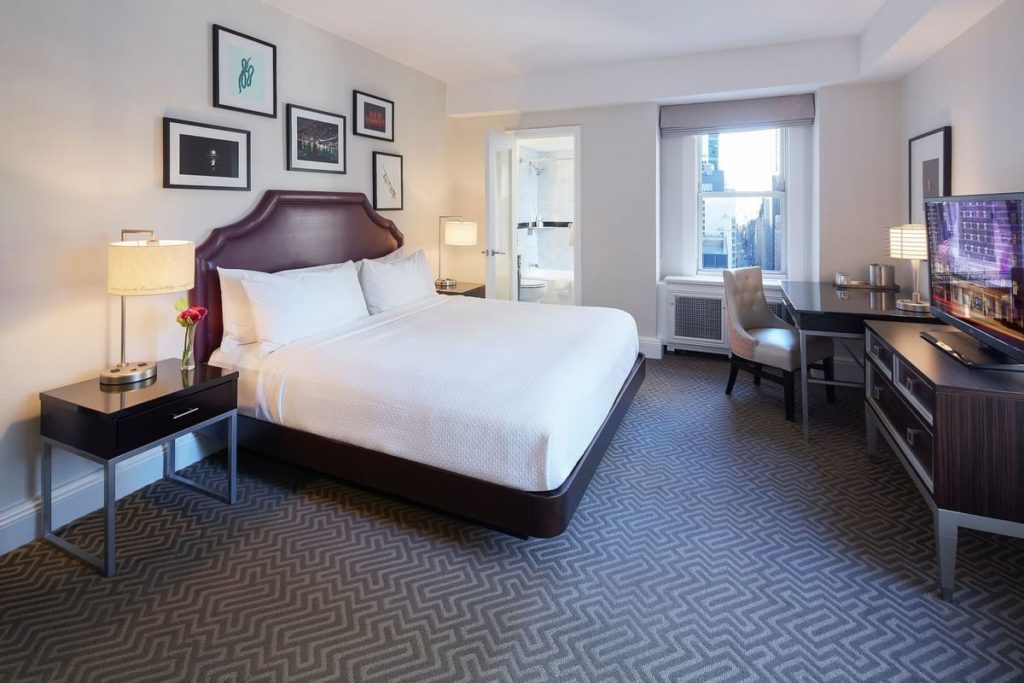 Elegant hotel room at The Lexington Hotel, Autograph Collection in New York, showcasing a large bed, framed artwork, and a desk area near a window with city views, ideal for US Open accommodations.