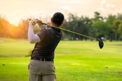 A golfer in action, swinging a driver on a sunny day, captures the essence of the premier golf event, the Masters Tournament in Augusta, GA.