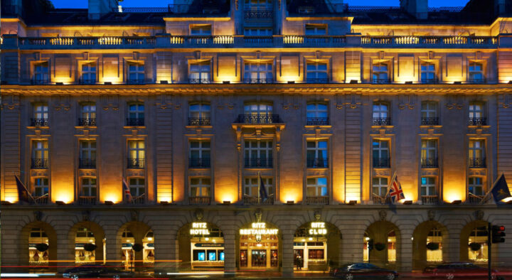 Exterior view of a luxury hotel in London at twilight, illuminated with warm lights, showcasing its elegant architecture and vibrant street environment, ideal accommodation for visitors to the Wimbledon Championships.