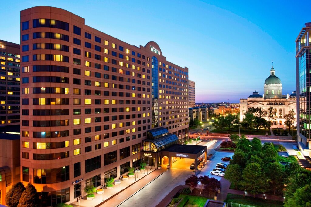 Westin hotel exterior at twilight with lights on, facing a street leading to the dome-topped State Capitol in Indianapolis, ideal for visitors of the Indianapolis 500.