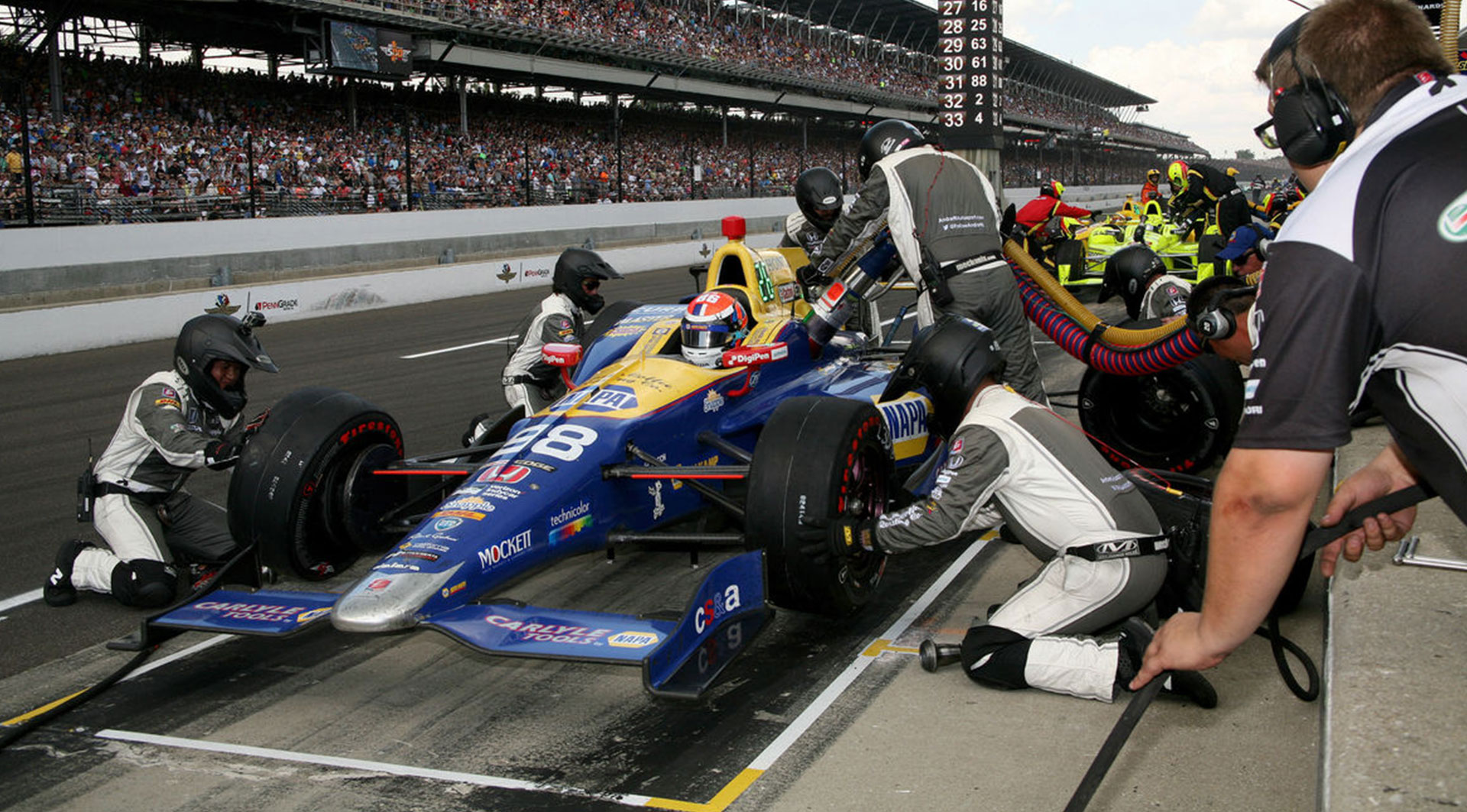 A professional pit crew works efficiently on a blue and yellow race car during the Indianapolis 500, providing a glimpse into the behind-the-scenes action of this iconic event.