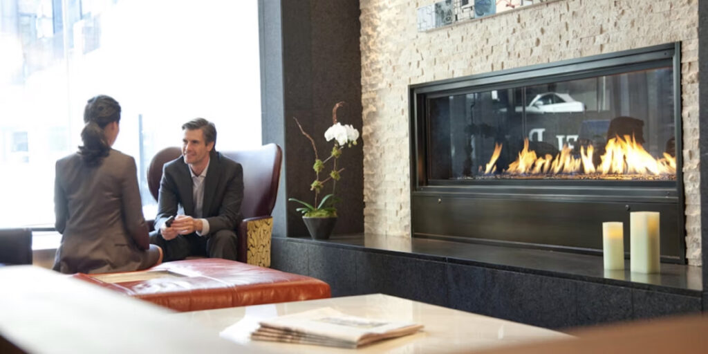 Two people converse by a fireplace in the lobby of InterContinental New York Times Square, a popular choice for luxury Ryder Cup accommodations in New York.
