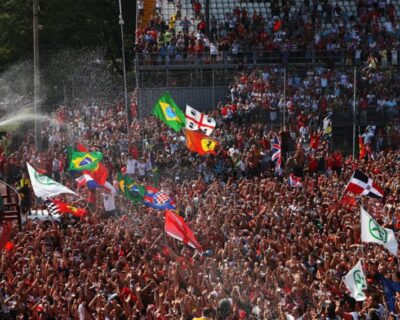 Race car driver celebrates by spraying champagne over an ecstatic crowd waving flags at the Italian Grand Prix, capturing the excitement of this iconic motorsport event.