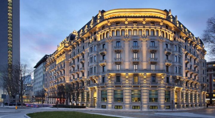 An opulent, illuminated hotel building captured at dusk, representing the luxury accommodations featured in the Italian Grand Prix travel packages.