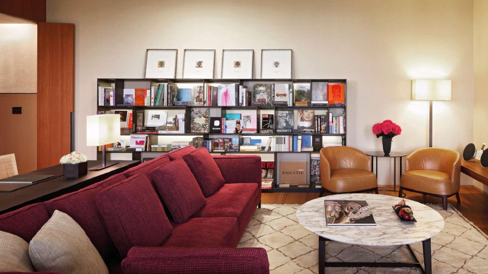 Luxury suite at the Bvlgari Hotel Milano, showcasing a cozy seating area with a red couch, book-filled shelves, and elegant decor, ideal for guests visiting the Italian Grand Prix in Milan.