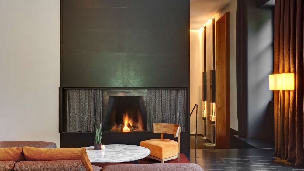 Elegant hotel lounge area with a cozy lit fireplace, plush seating, and warm lighting, located at Bvlgari Hotel Milano, an accommodation choice for Italian Grand Prix visitors in Milan.