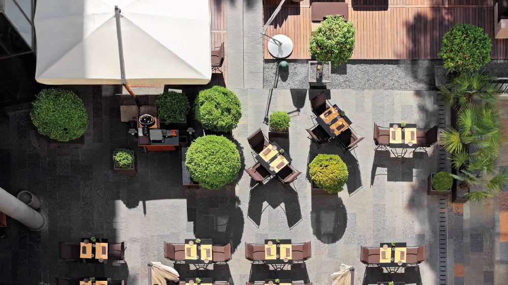 Top-down view of an outdoor dining area at Bvlgari Hotel Milano, showcasing tables set for service, umbrellas for shade, and lush greenery, ideal for guests visiting during the Italian Grand Prix.