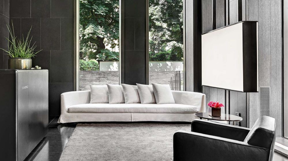 Modern living room at Bvlgari Hotel Milano, showing a sleek white sofa, black chairs, and a large window overlooking greenery, ideal for guests visiting the Italian Grand Prix in Milan.