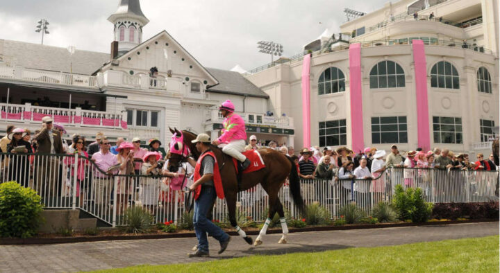 A jockey on a horse walks past a crowd of spectators at the Kentucky Derby, showcasing optional add-ons like the Mint Julep Sunset Social and Kentucky Oaks.